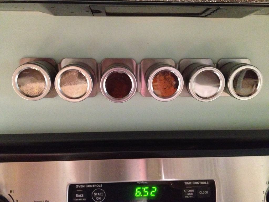 A photo of the finished magnetic spice rack, with jars of various spices attached. Common baking ingredient are easy to access.