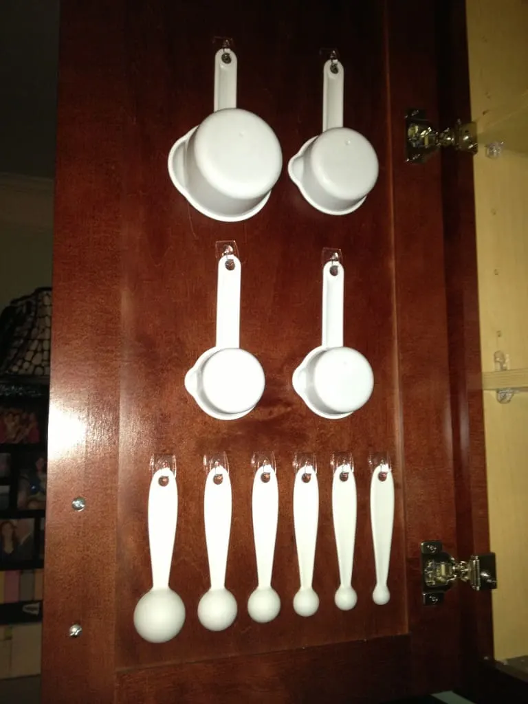 A photo of the inside of the baking cabinet door, with measuring spoons hanging from command hooks.