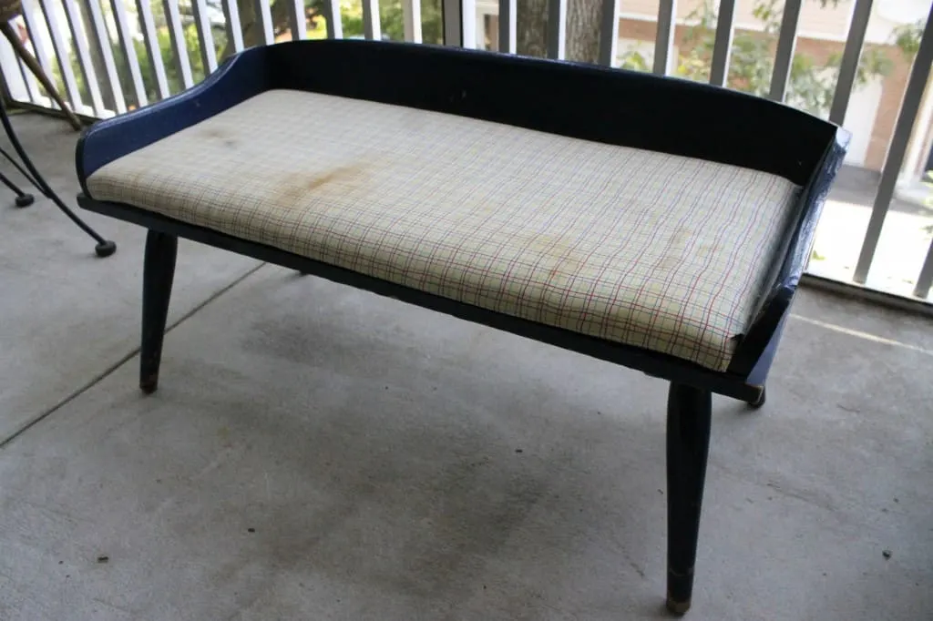 A photo of the bench before it was reupholstered. The bench seat's fabric is stained. 