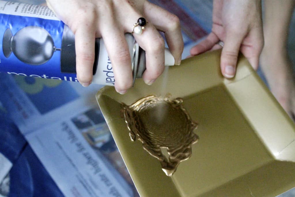 A photo of gold spray paint being sprayed into a tray. 