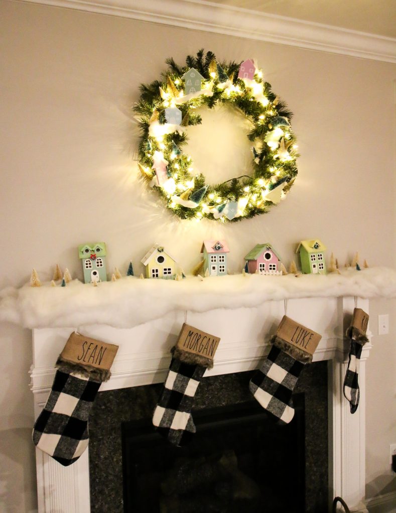 pastel wooden houses on a mantel with buffalo check stockings