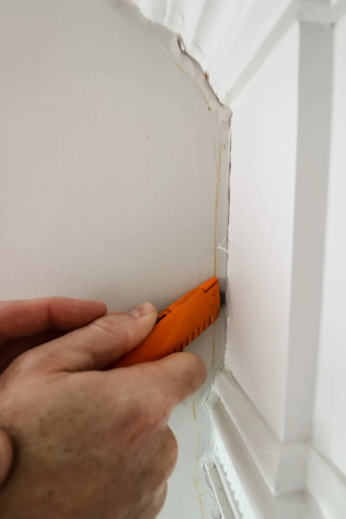 Using utility knife to cut caulk from fireplace