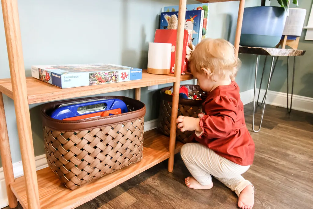 Toddler getting toys off of dowel rod bookshelf