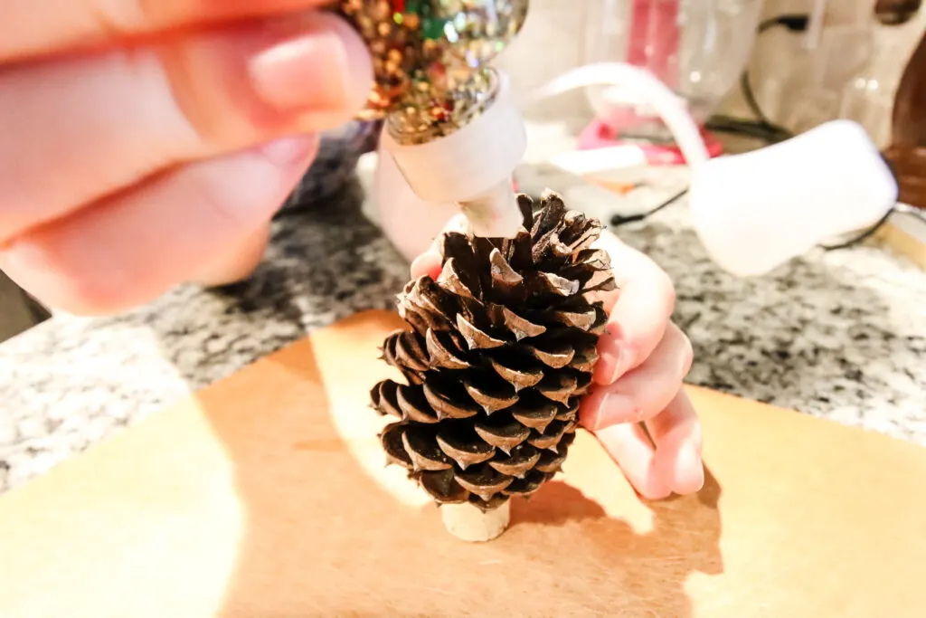 adding glitter to a pine cone