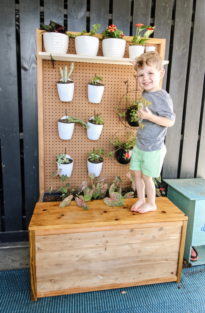 child standing on a bench with a pegboard plant holder