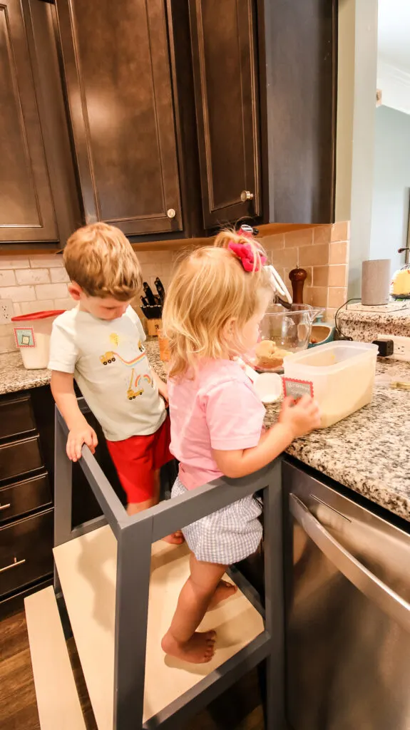 Kids standing on learning tower while baking