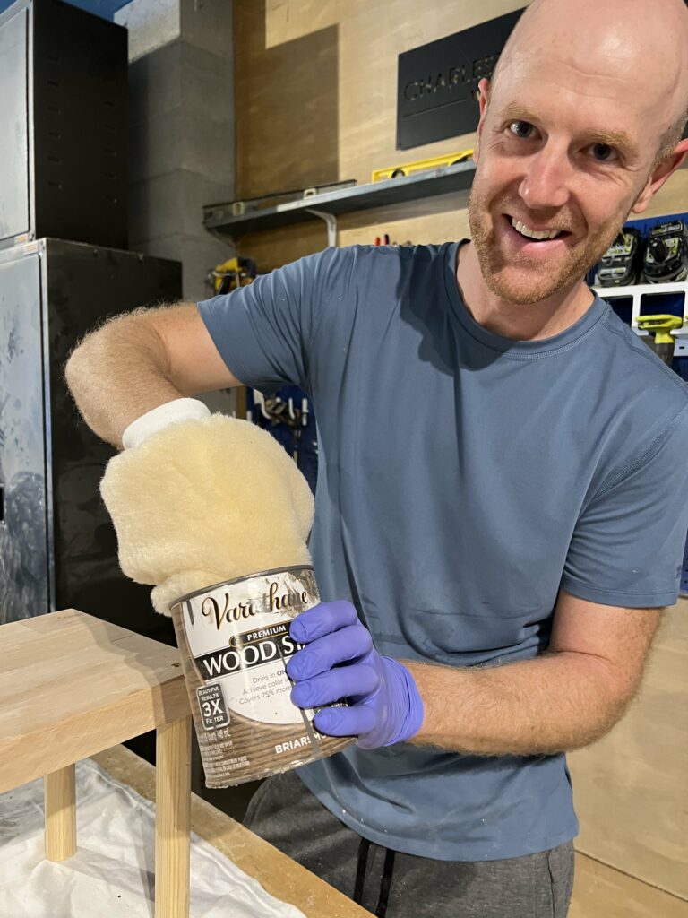 supertuff paint mitt on hand dipping into a can of wood stain