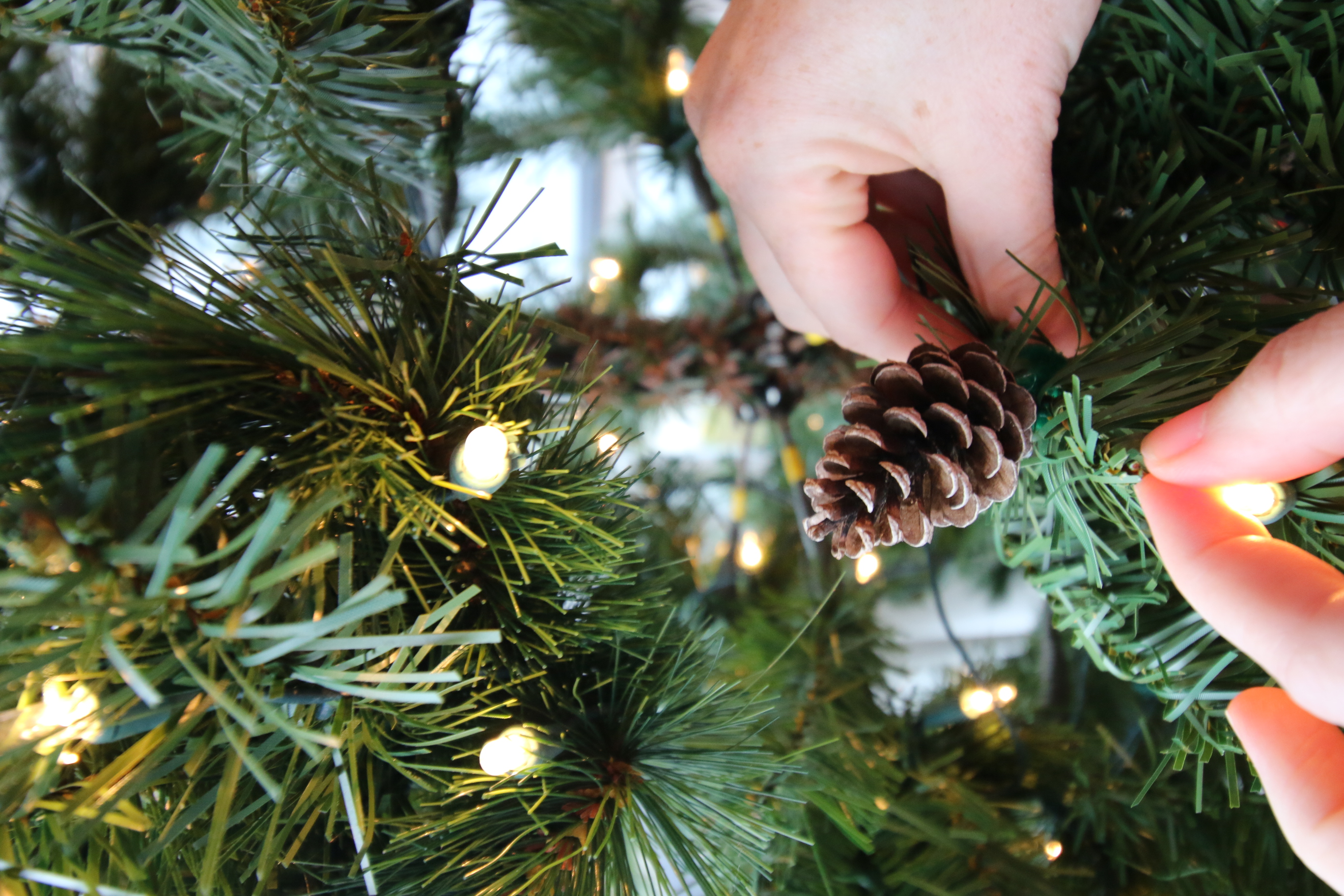 attaching a pine cone to a christmas tree branch with wire