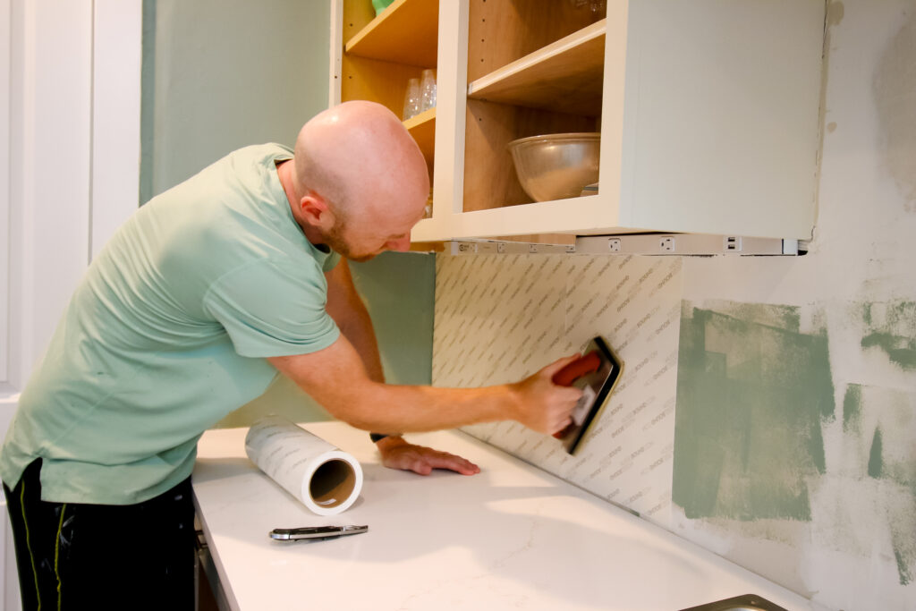 pressing cutting musselbound peel and stick adhesive sheets into the wall with a grout float